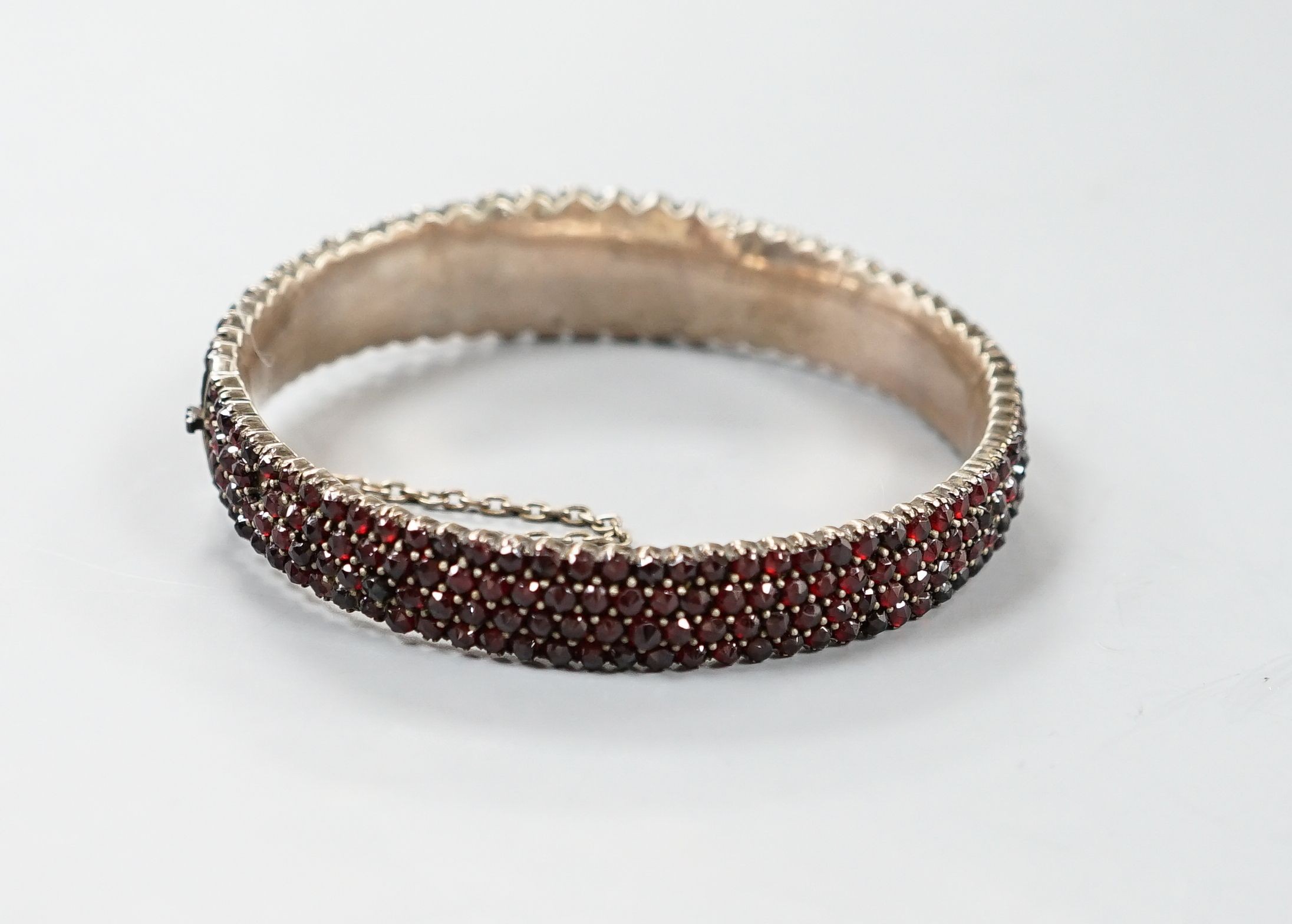 A late Victorian gilt white metal and garnet encrusted hinged bangle (stone missing).